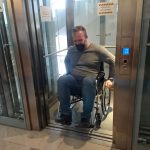 Na zdjęciu otwarta winda, z niej wyjeżdżający mężczyzna na wózku inwalidzkim. Mężczyzna uczestniczy w szkoleniu, doświadcza niepełnosprawności.