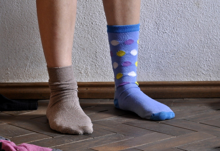 Męskie stopy, na których założone są dwie różne skarpetki: jedna brązowa, druga niebieska w kropki.